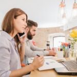 kobieta i mężczyzna siedzący w biurze, ona rozmawia przez telefon, on coś notuje
