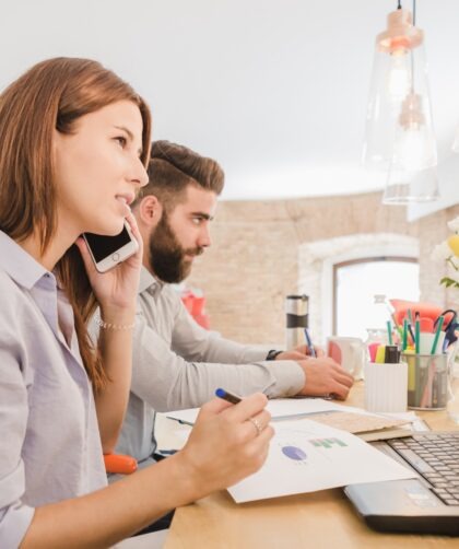 kobieta i mężczyzna siedzący w biurze, ona rozmawia przez telefon, on coś notuje