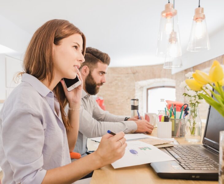 kobieta i mężczyzna siedzący w biurze, ona rozmawia przez telefon, on coś notuje
