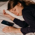 śpiąca kobieta i leżący obok smartfon z włączoną funkcją drzemki