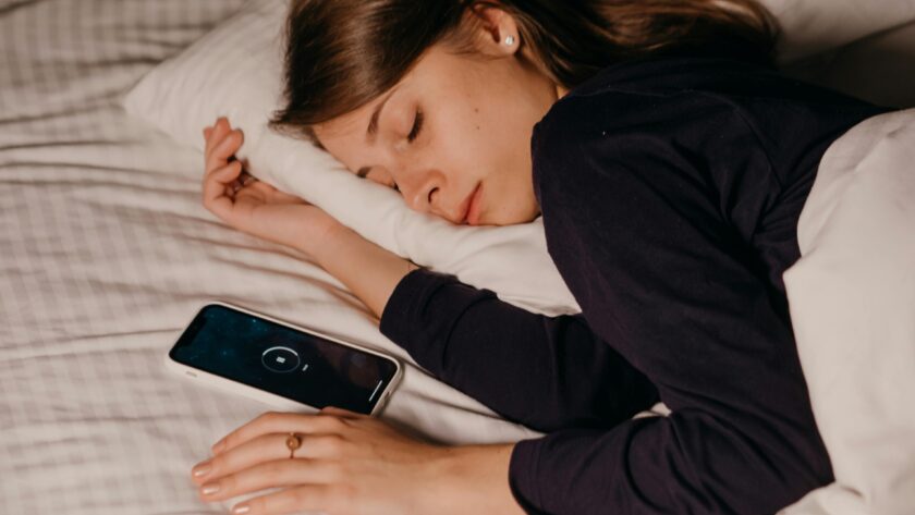 śpiąca kobieta i leżący obok smartfon z włączoną funkcją drzemki