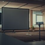 Mobilny ekran projekcyjny na kółkach oraz projektor na statywie w sali konferencyjnej