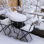 Stolik i dwa krzesła na tarasie pokryte grubą warstwą śniegu
