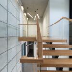 Drewniane schody z przeszkloną balustradą przy ścianie z surowego betonu