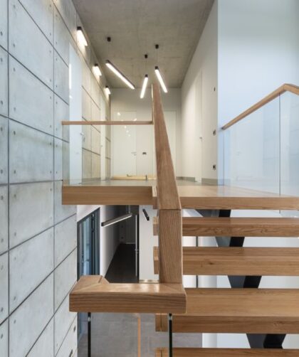 Drewniane schody z przeszkloną balustradą przy ścianie z surowego betonu