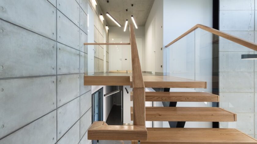Drewniane schody z przeszkloną balustradą przy ścianie z surowego betonu