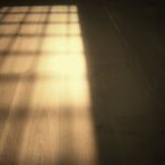 Cień okiennej kratki rzucany przez słońce na jasną drewnianą podłogę