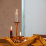 Płonące świece w mosiężnych świecznikach ustawione na żółtej tkaninie